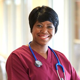 Lachende verpleegkundige in bordeauxrode beroepskleding met een 3M Littmann Classic III Stethoscope met blauwe buizen.